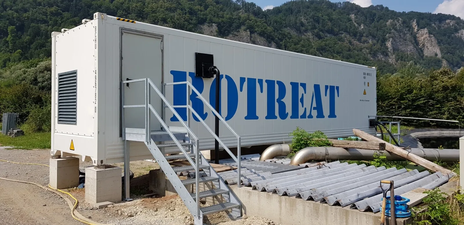 White Rotreat plant container with stairs in front of wooded mountains, pipes to the basin